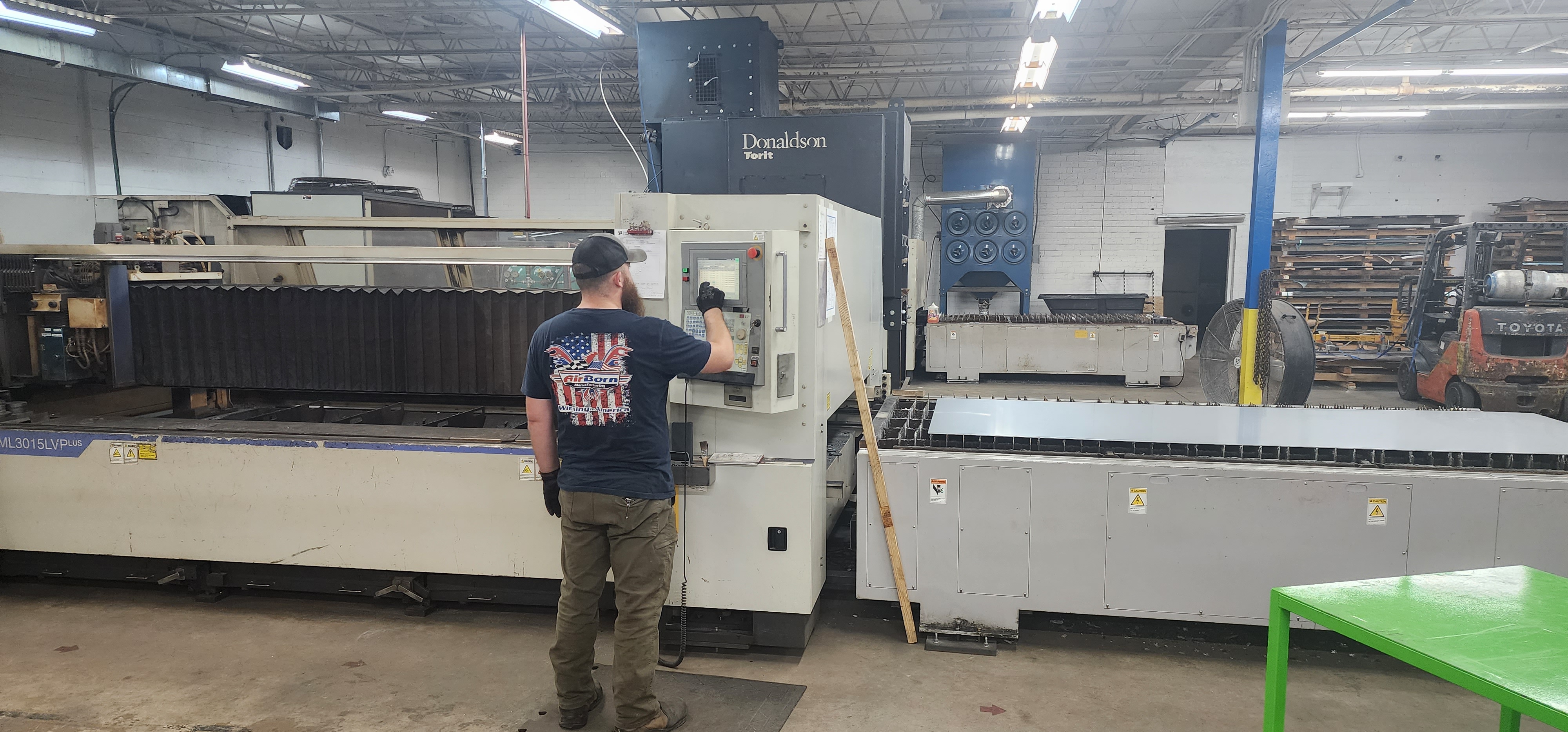 Operator standing near a CNC laser cutting machine in the AirBorn Manufacturing shop.