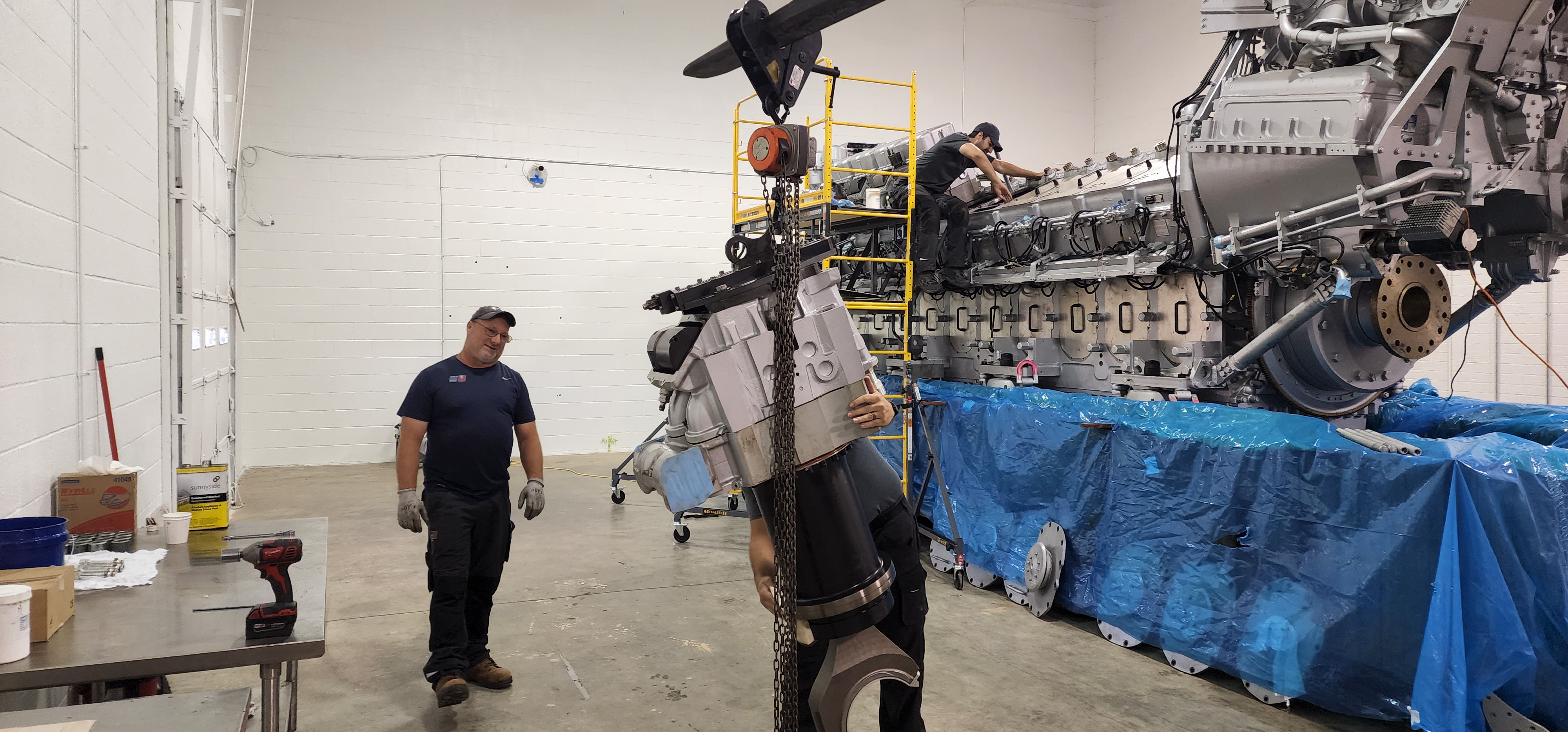 Crane-assisted handling of a large engine component in a shop.