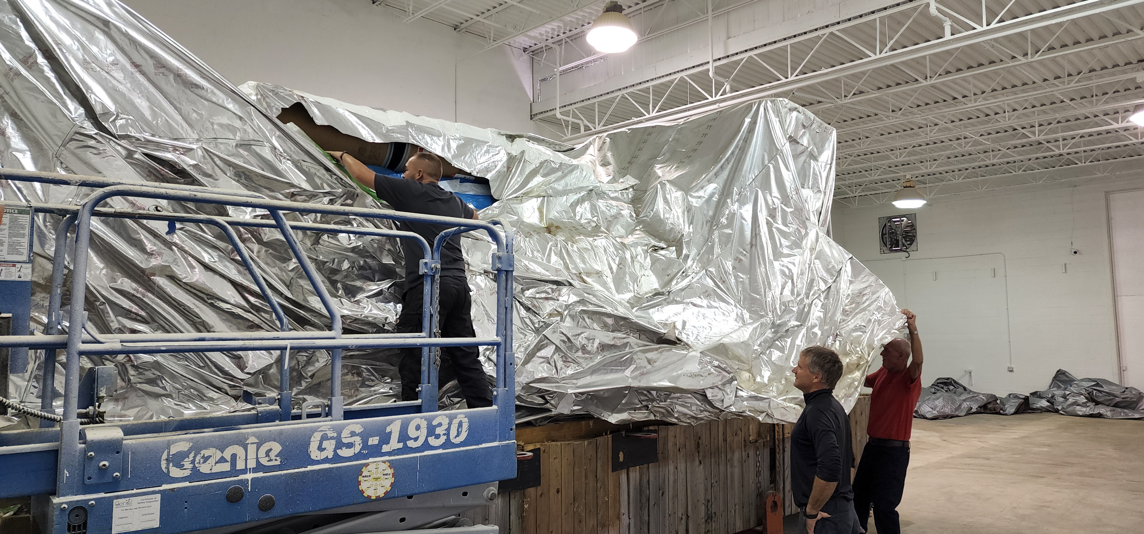 Crane handling a wrapped fabricated component during loading preparation.