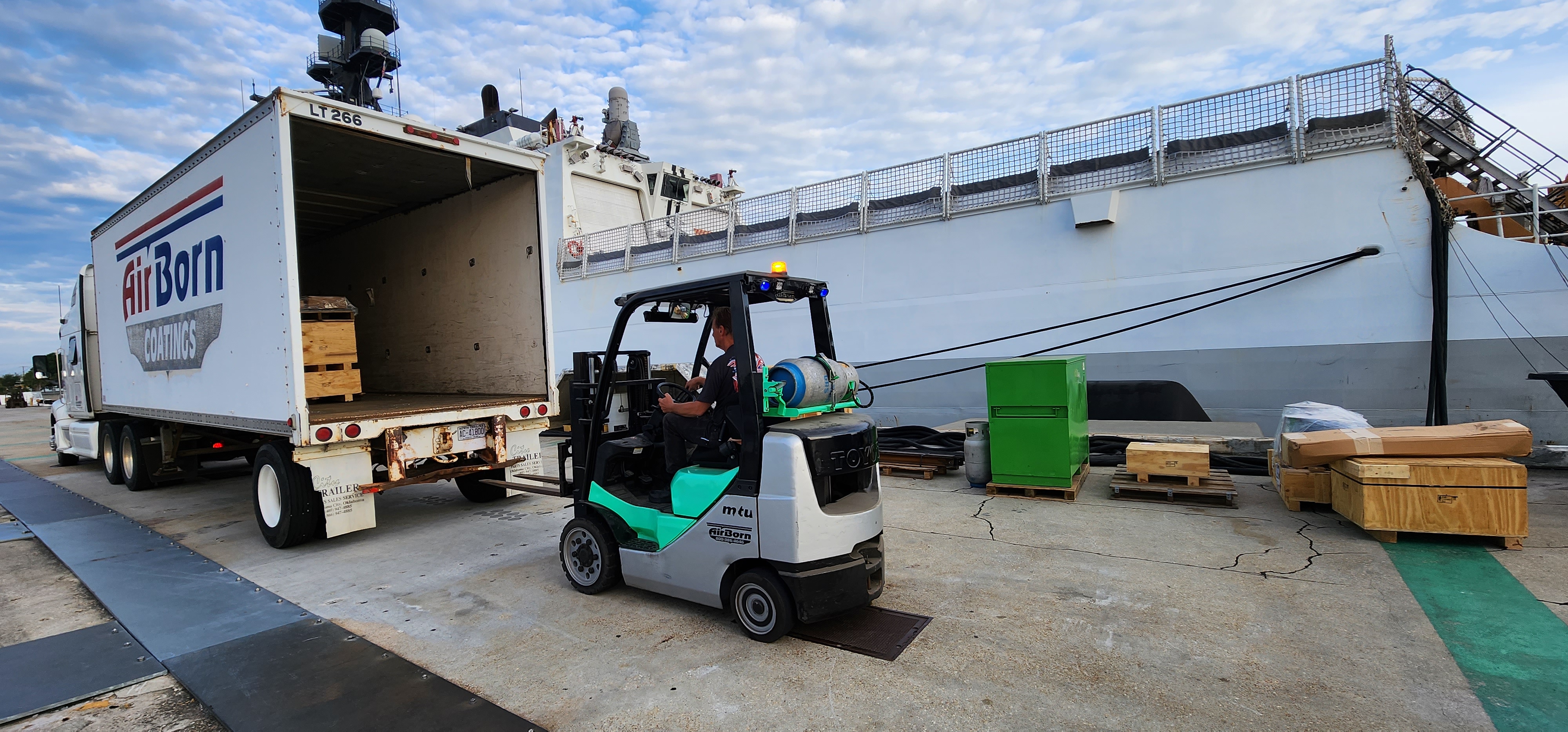 Forklift loading fabricated metal components near a truck for shipment.