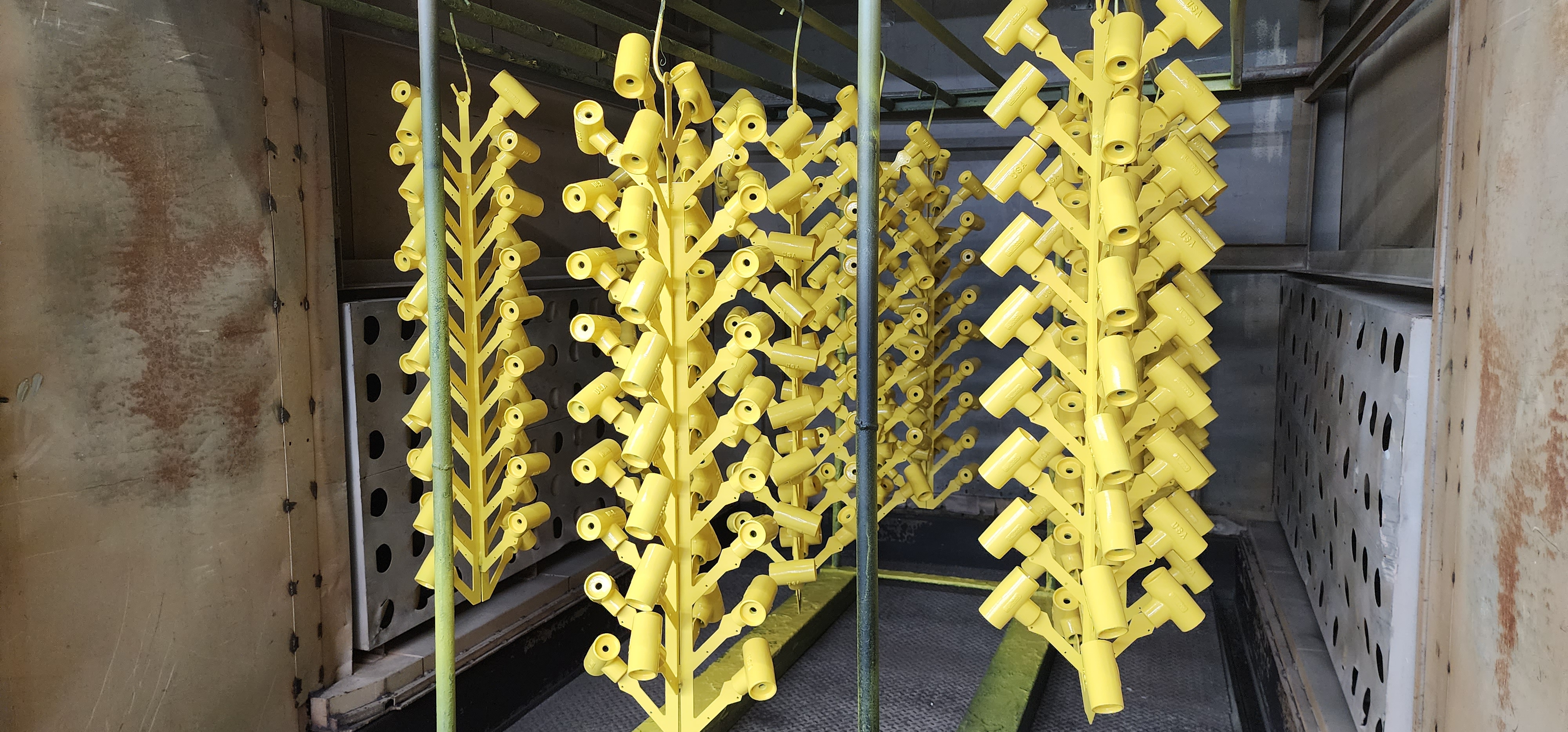 Yellow finished metal brackets staged on a rack after coating.