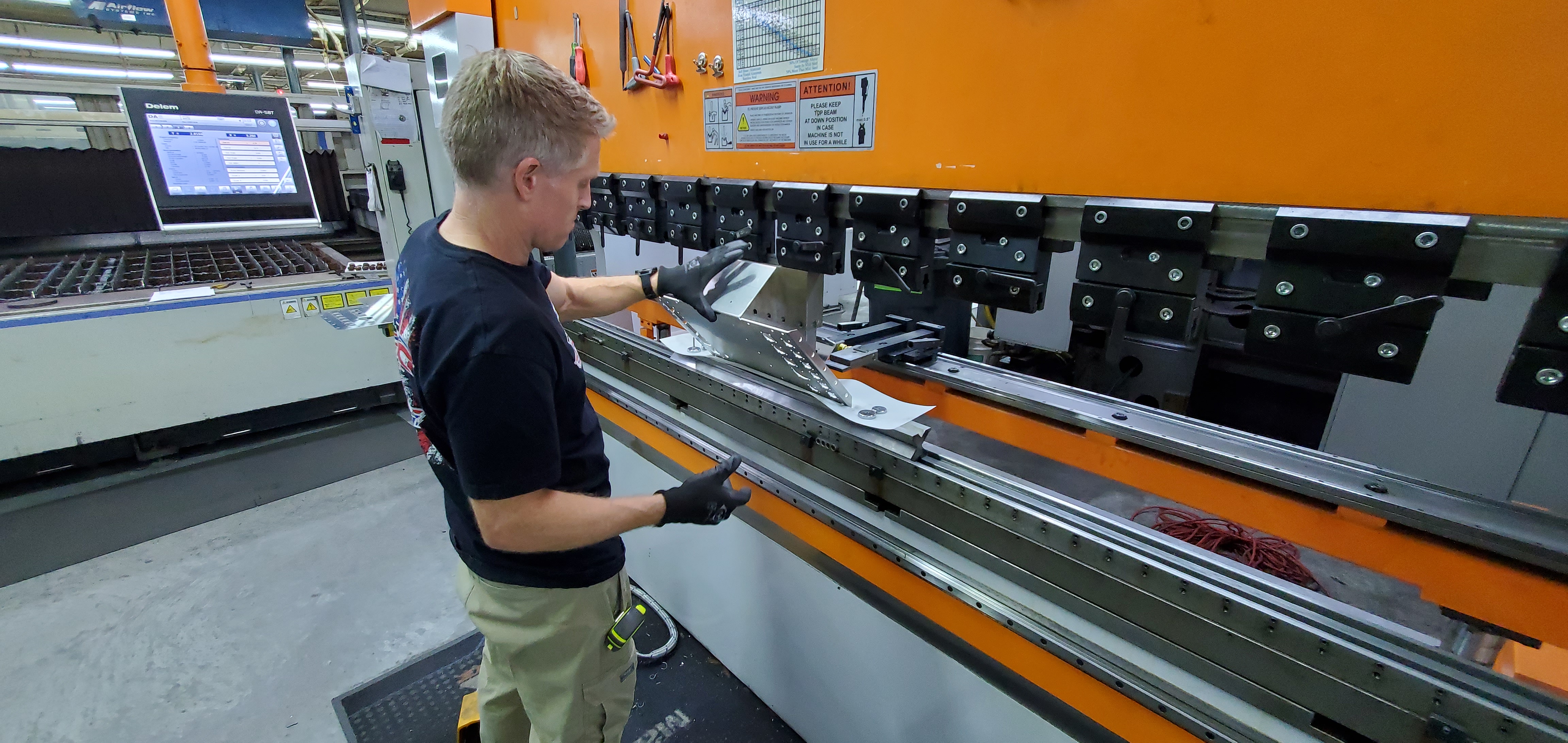 Technician forming a long metal panel on press brake equipment.