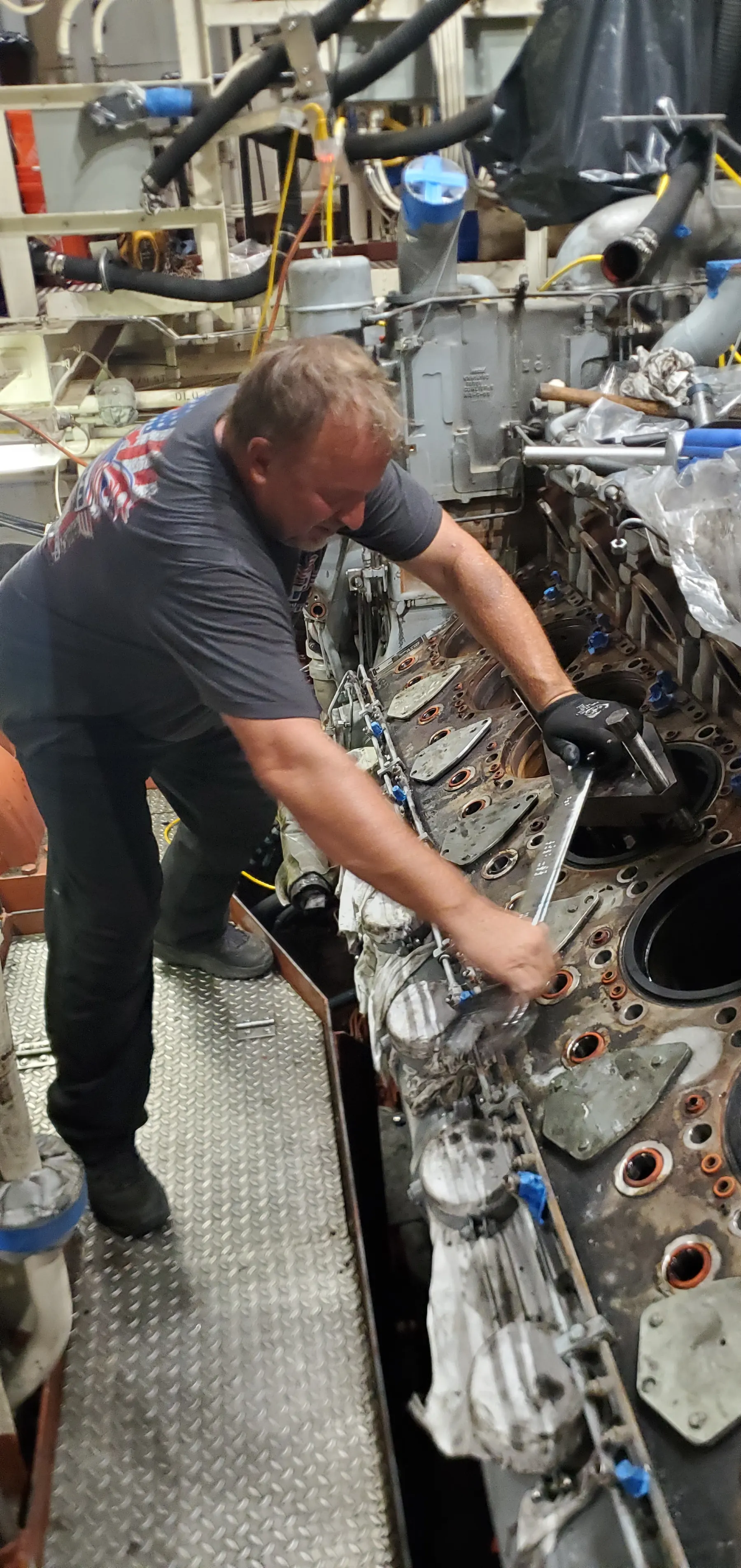 Technician working underneath a large engine assembly with tools and access equipment.