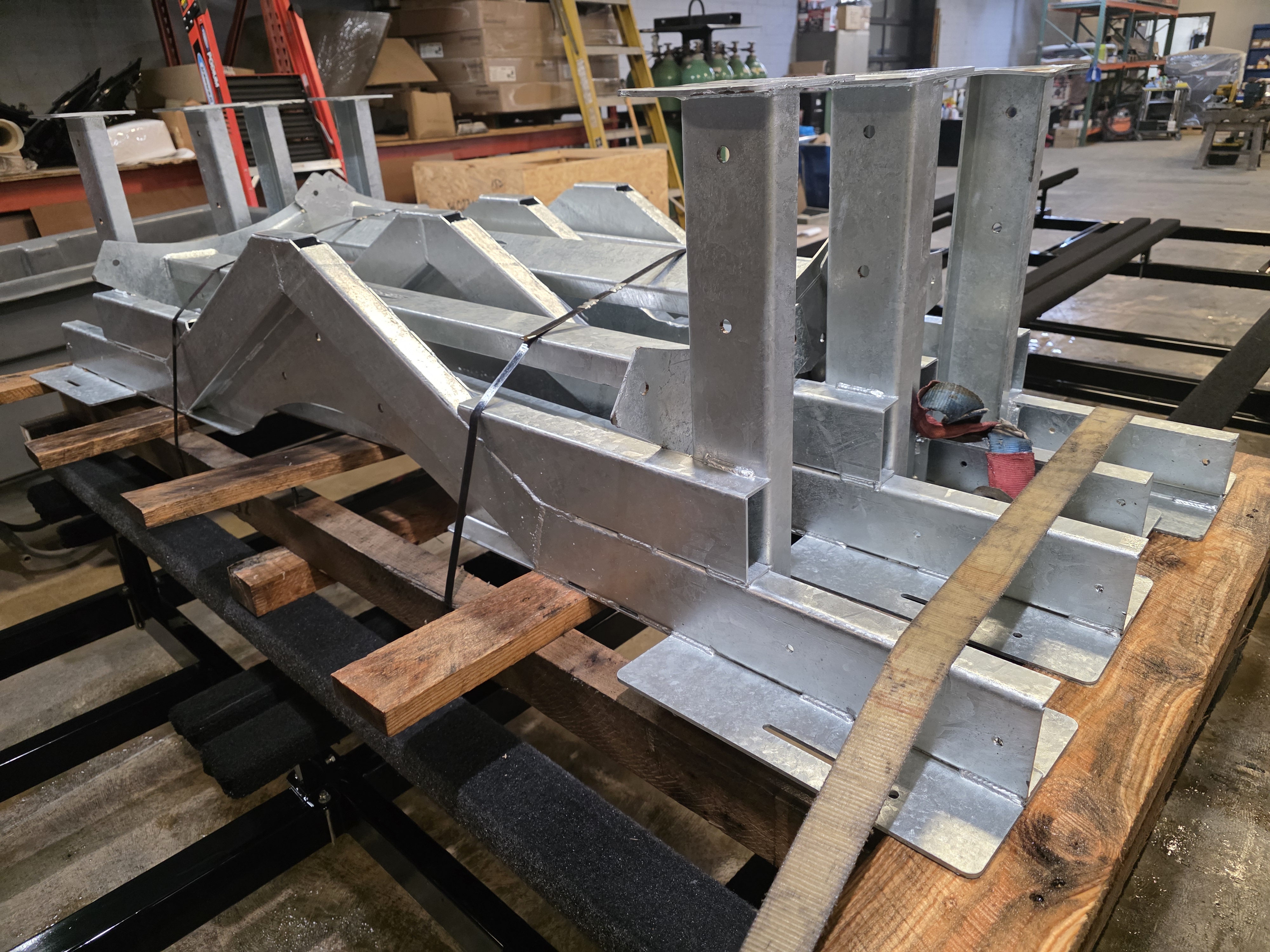 Welded aluminum frame assembly with production components staged nearby.